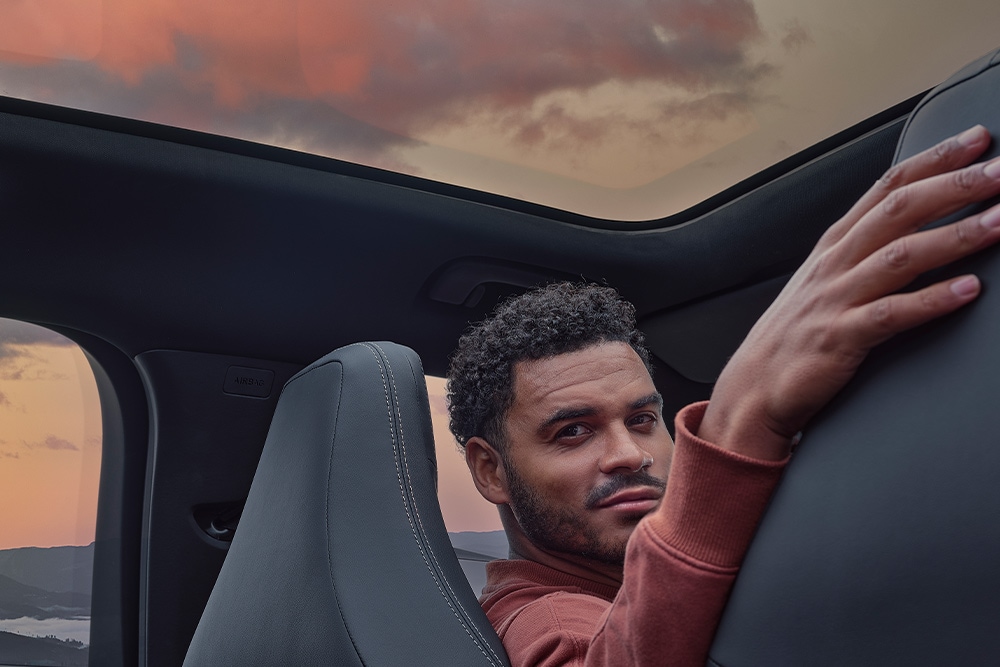 Ein Mann sitzt bei Sonnenuntergang in einem Auto, seine Hand liegt auf der Rückenlehne eines der Sitze.