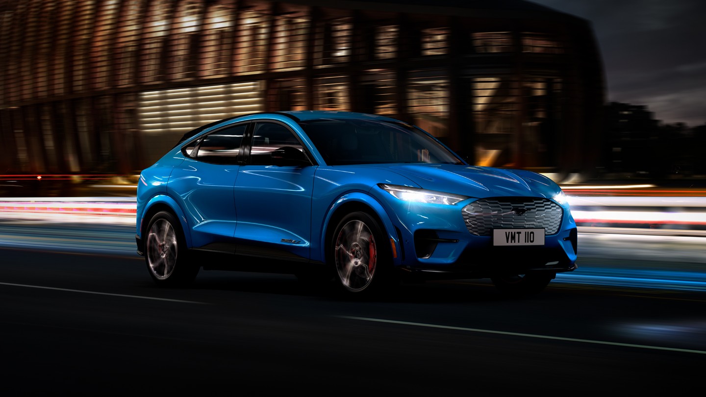 Ford Mustang Mach-E in Blau. Dreiviertelansicht, auf einer Straße fahrend bei Nacht
