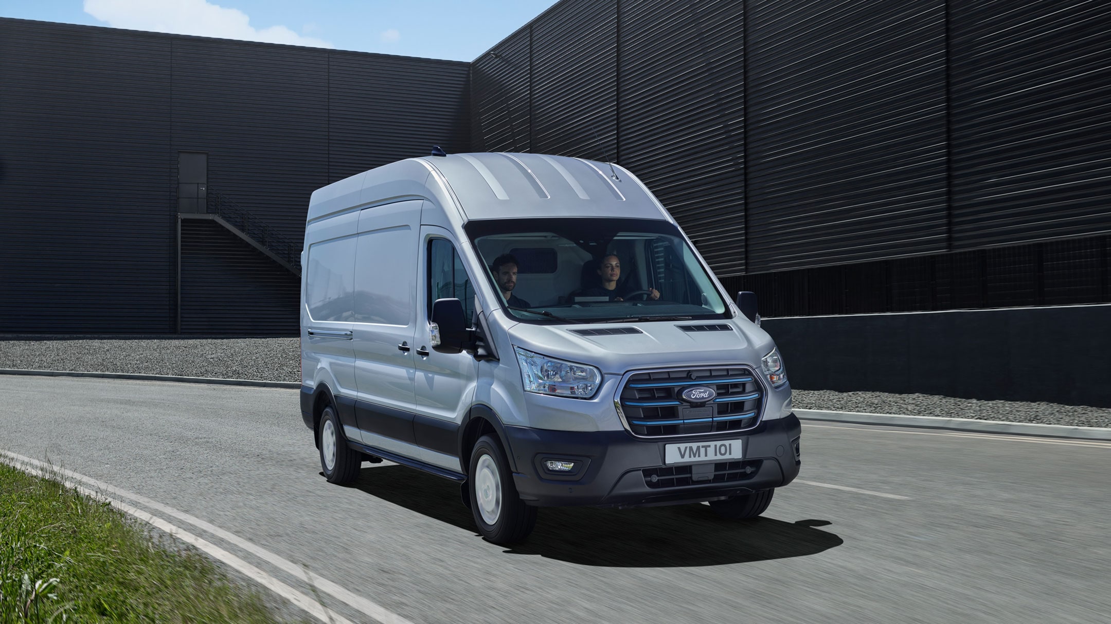 Ford E-Transit in Silber. Frontansicht, auf einer Straße fahrend