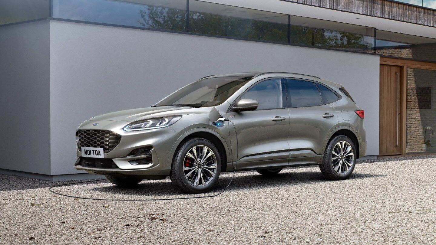 Ford Kuga in Grau. Dreiviertelansicht, parkend vor Wohnhaus beim Aufladen