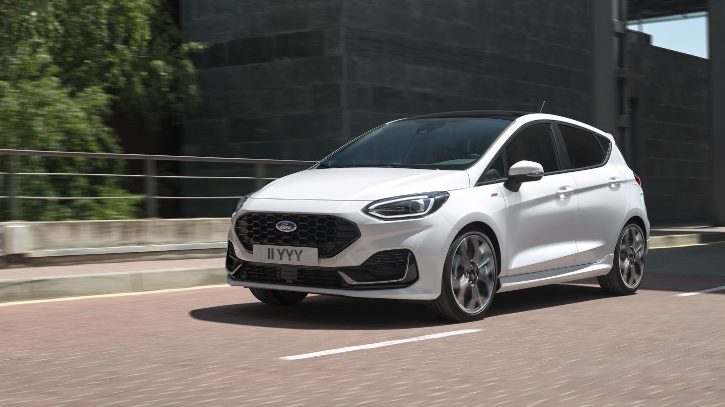 Ford Fiesta in Weiß. Dreiviertelansicht, auf einer Straße fahrend Ford Fiesta in Weiß. Dreiviertelansicht, auf einer Straße fahrend