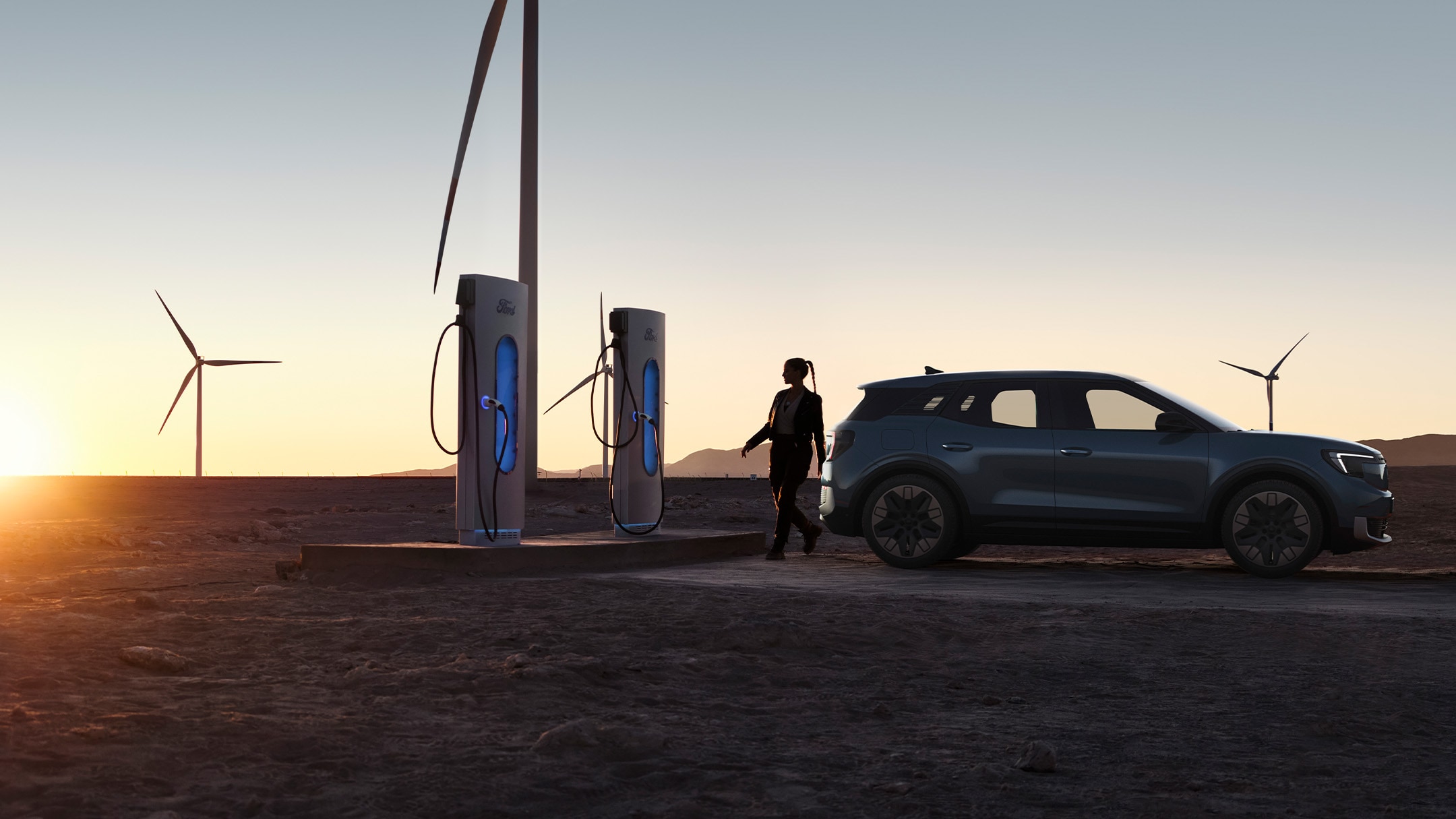 Der vollelektrische Ford Explorer in Blau. Seitenansicht, parkend bei einer Ladestation bei Sonnenuntergang.