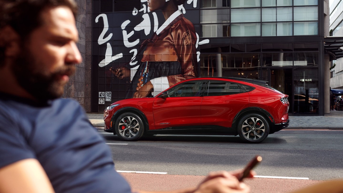 Ein Mann blickt auf sein Telefon mit einem geparkten roten Ford Elektrofahrzeug