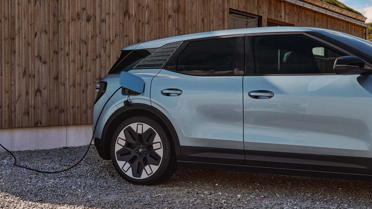Der vollelektrische Ford Explorer in Blau. Seitenansicht, parkend an einer Ladestation. 