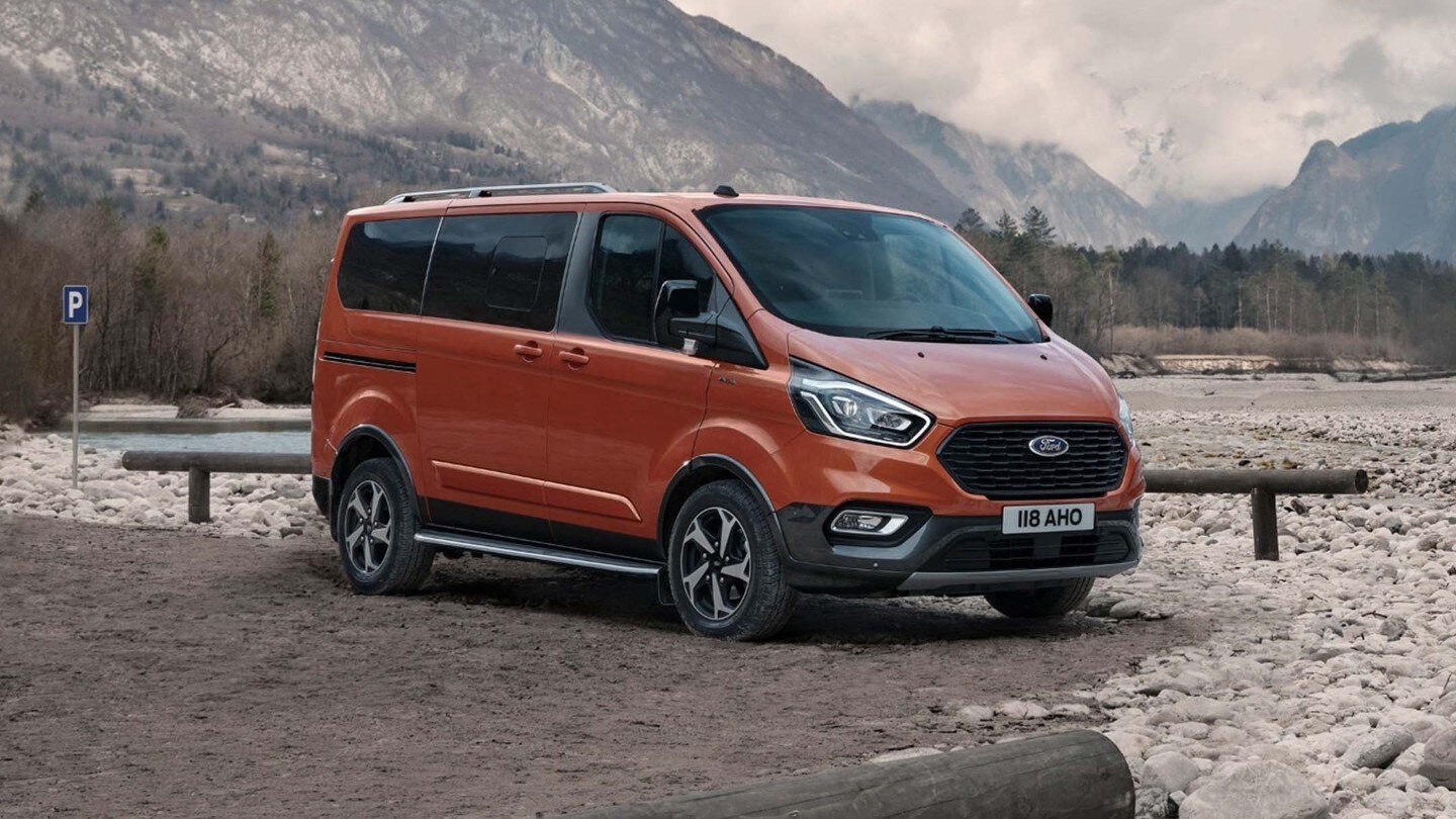 Ford Tourneo Custom in Orange. Dreiviertelansicht, auf Kies geparkt