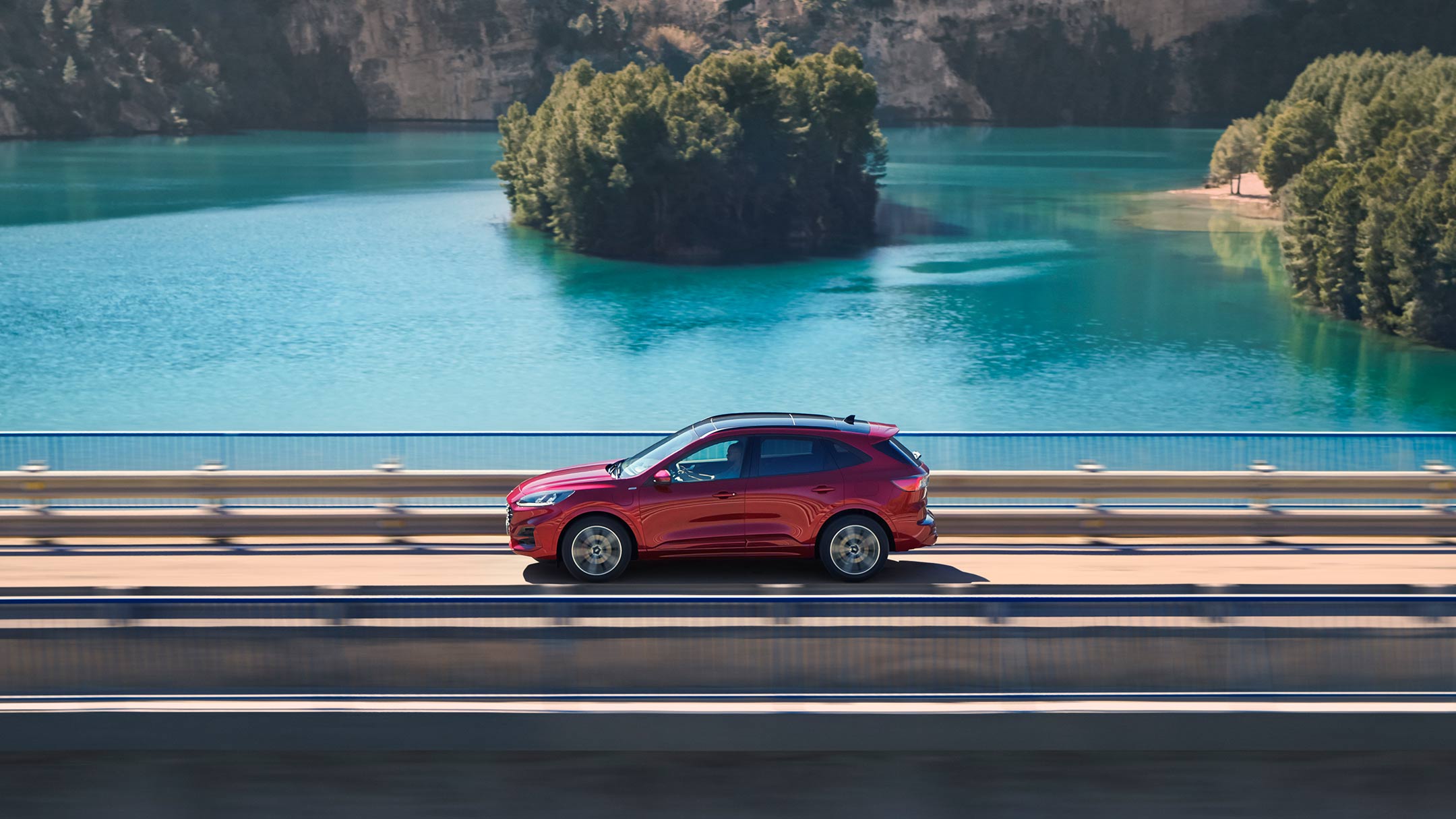 Ford Kuga in Rot. Seitenansicht, fahrend auf einer Brücke.