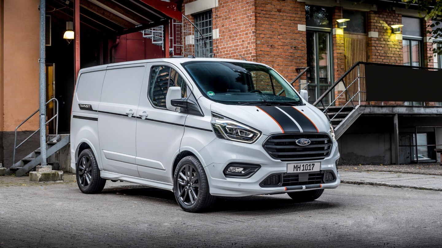 Ford Transit Custom in Weiß. Dreiviertelansicht, vor einer Halle parkend