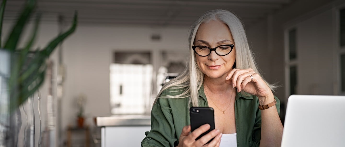 Frau sitz an einem Schreibtisch und hält Mobiltelefon in der Hand