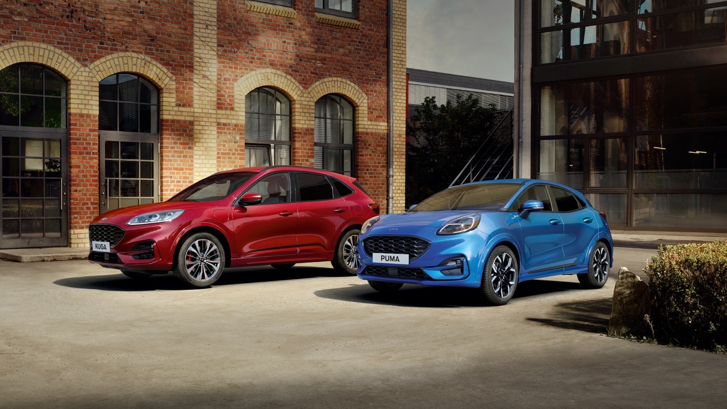 Ford Puma in Blau und Ford Kuga in Rot. Dreiviertelansicht, vor einem Gebäude geparkt