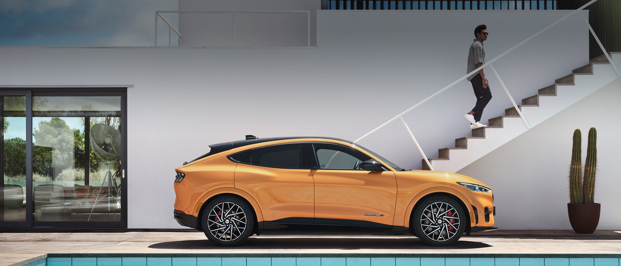 Ford Mustang Mach-E in Orange. Seitenansicht, parkt vor einem Haus