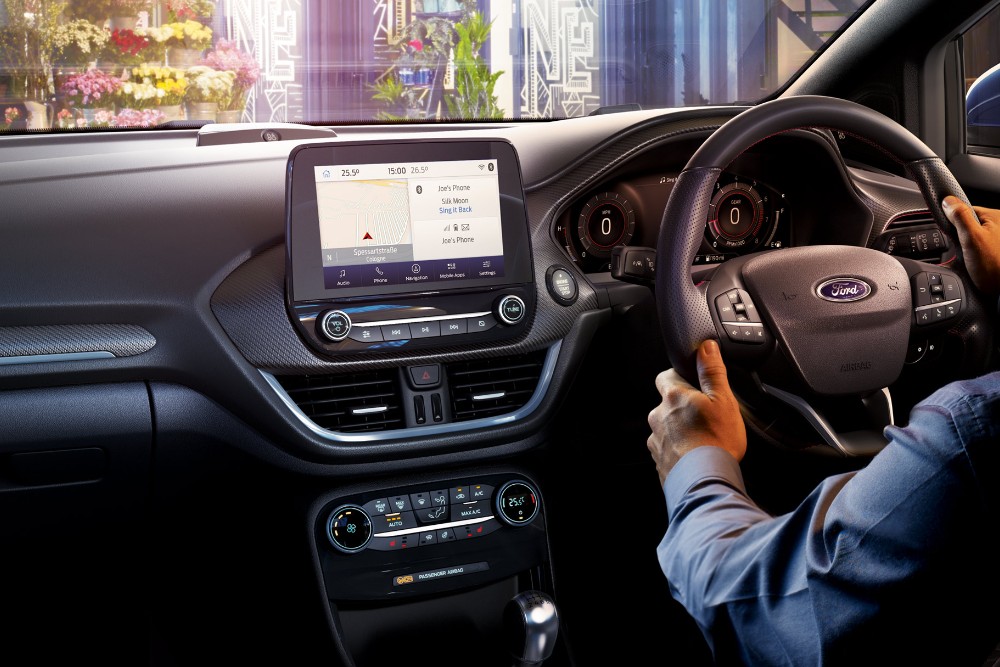 Interior of a Ford Puma with a person's hands on the steering wheel and a large touchscreen display.