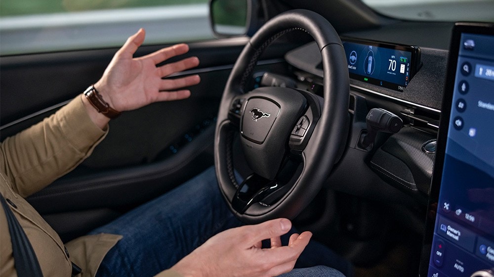 Eine Person sitzt im Fahrersitz eines Ford Mustang Mach-E und nimmt die Hände vom Lenkrad, um die BlueCruise-Technologie zu demonstrieren.