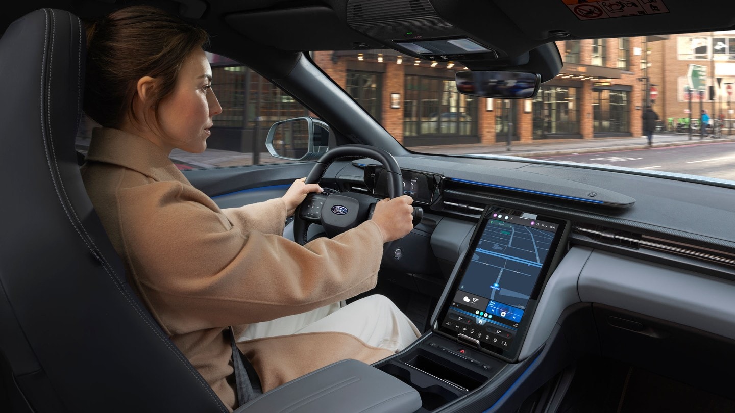Eine Person sitzt am Fahrersitz eines Ford Explorer, der auf einer Straße in einer Stadt fährt. 