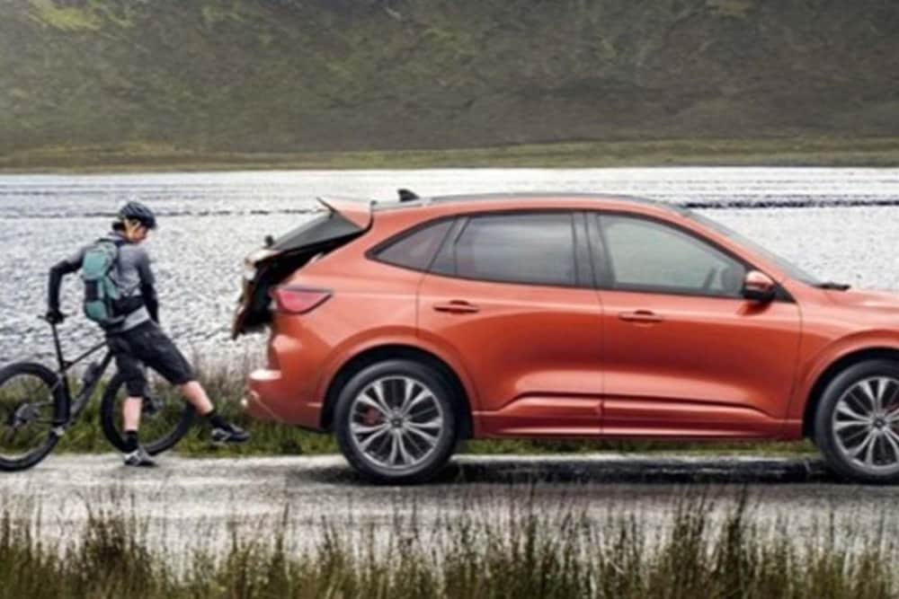 Ford Puma in Silber. Heckansicht, Frau öffnet sensorgesteuerte Heckklappe mit Fußbewegung