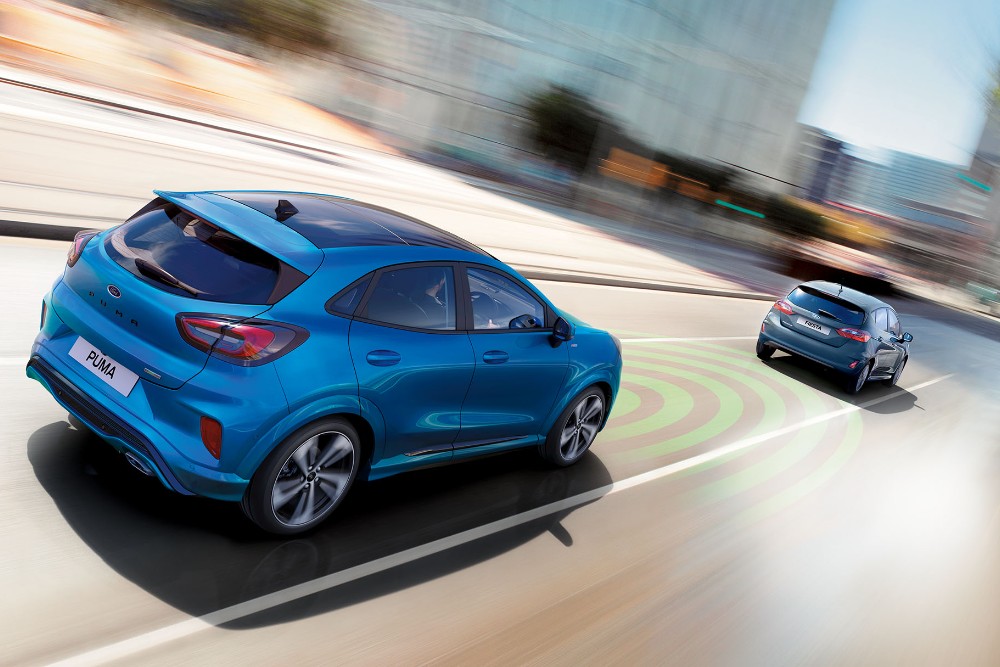Ford Puma in Blau. Heckansicht, auf einer Straße fahrend mit Visualisierung der adaptiven Geschwindigkeitsregelanlage