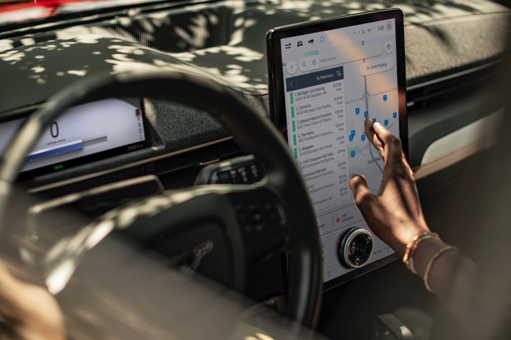 Ford Mustang Mach-E Innenraum. Person bedient den Touchscreen mit aktivierter Connected Navigation Funktion.