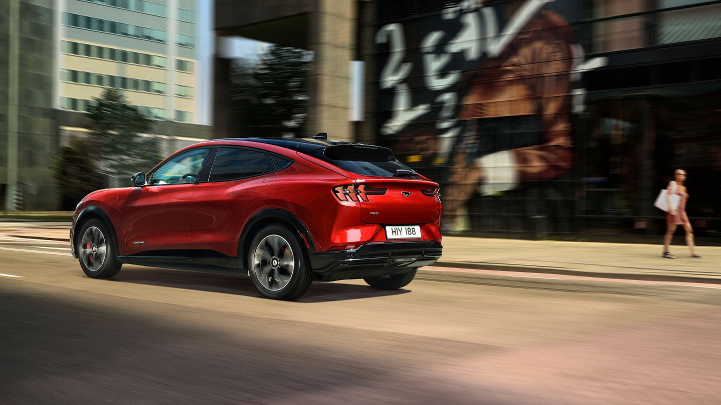 Ford Mustang Mach-E in Rot. Heckansicht, auf einer Straße fahrend