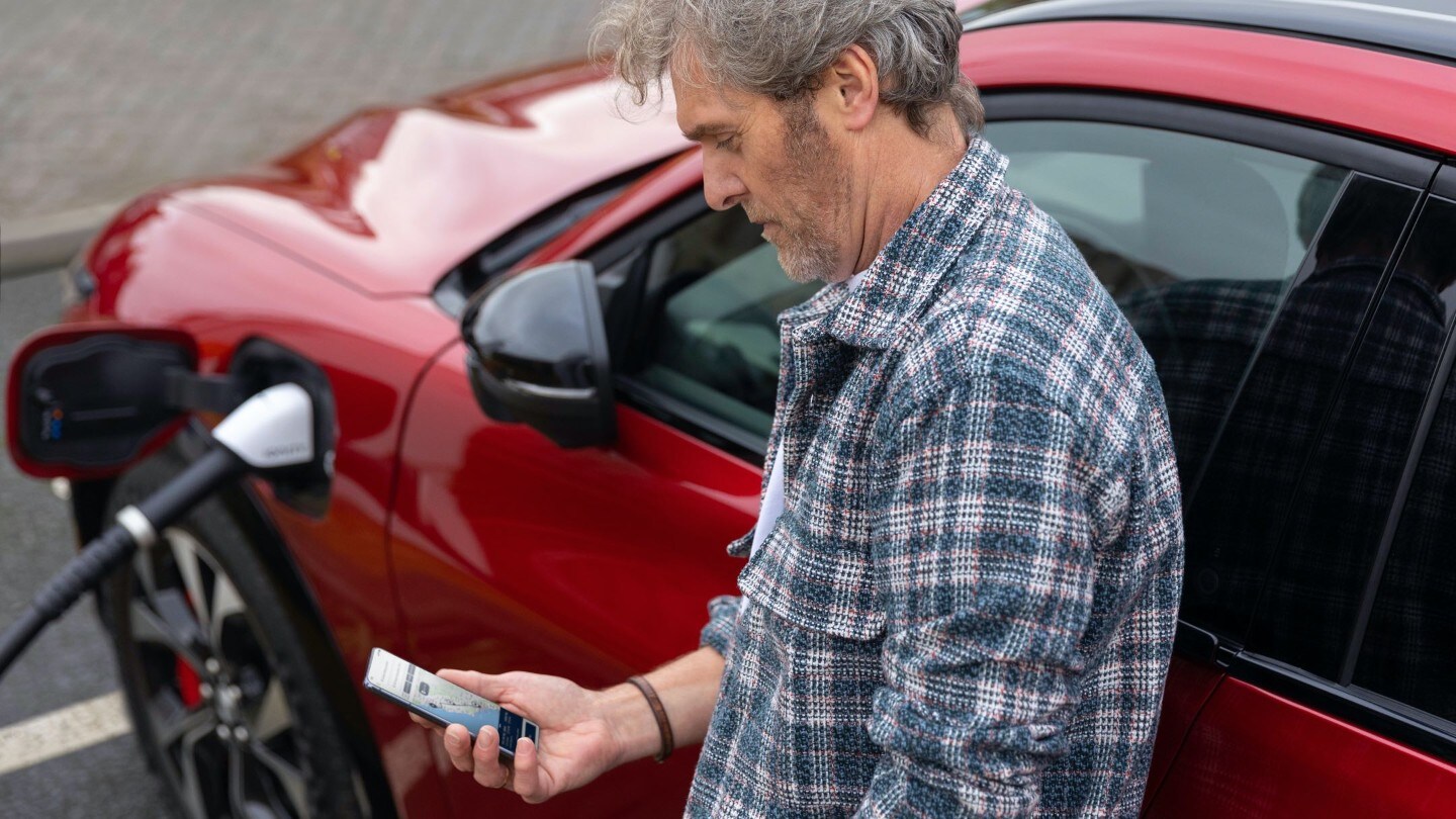 Plug & Charge, Mann sieht auf sein Smartphone während sein Auto auflädt