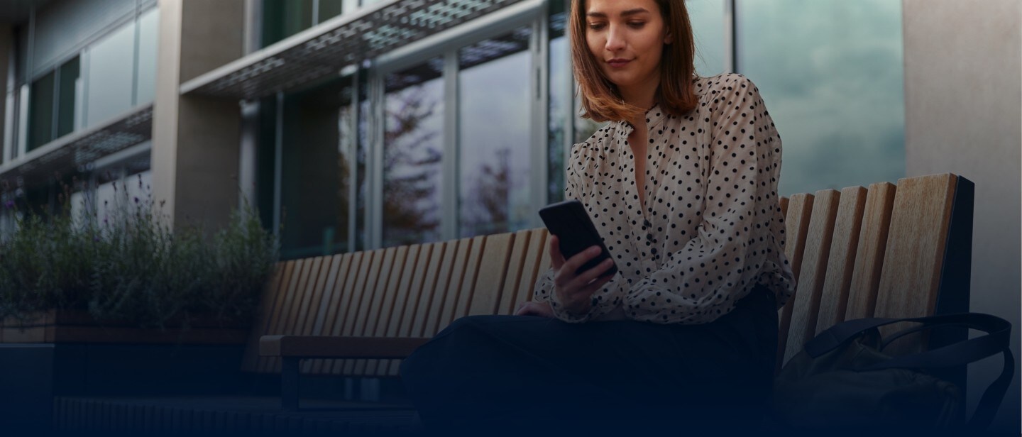 Frau sitzt auf einer Holzbank und hält ihr Smartphone in der Hand