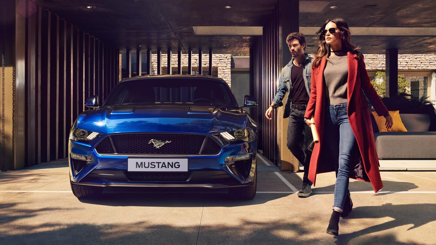 Ford Mustang in Blau. Frontansicht, parkend vor einem Metalltor