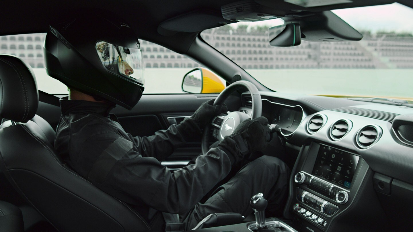 Ford Mustang. Innenansicht vom Beifahrersitz mit einem Rennfahrer am Steuer, der einen schwarzen Helm trägt 