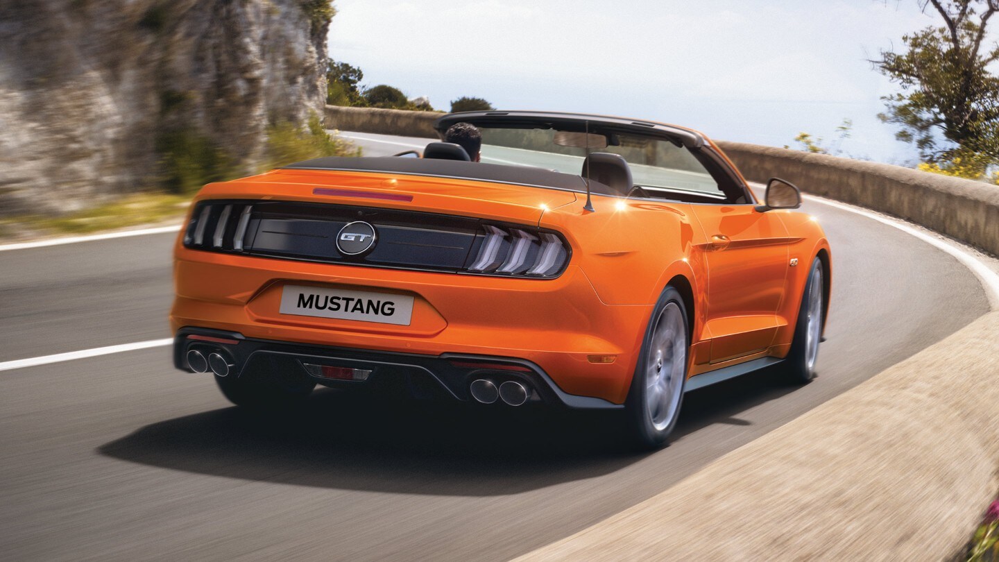 Ford Mustang in Orange. Heckansicht, fahrend durch eine Kurve im Gebirge