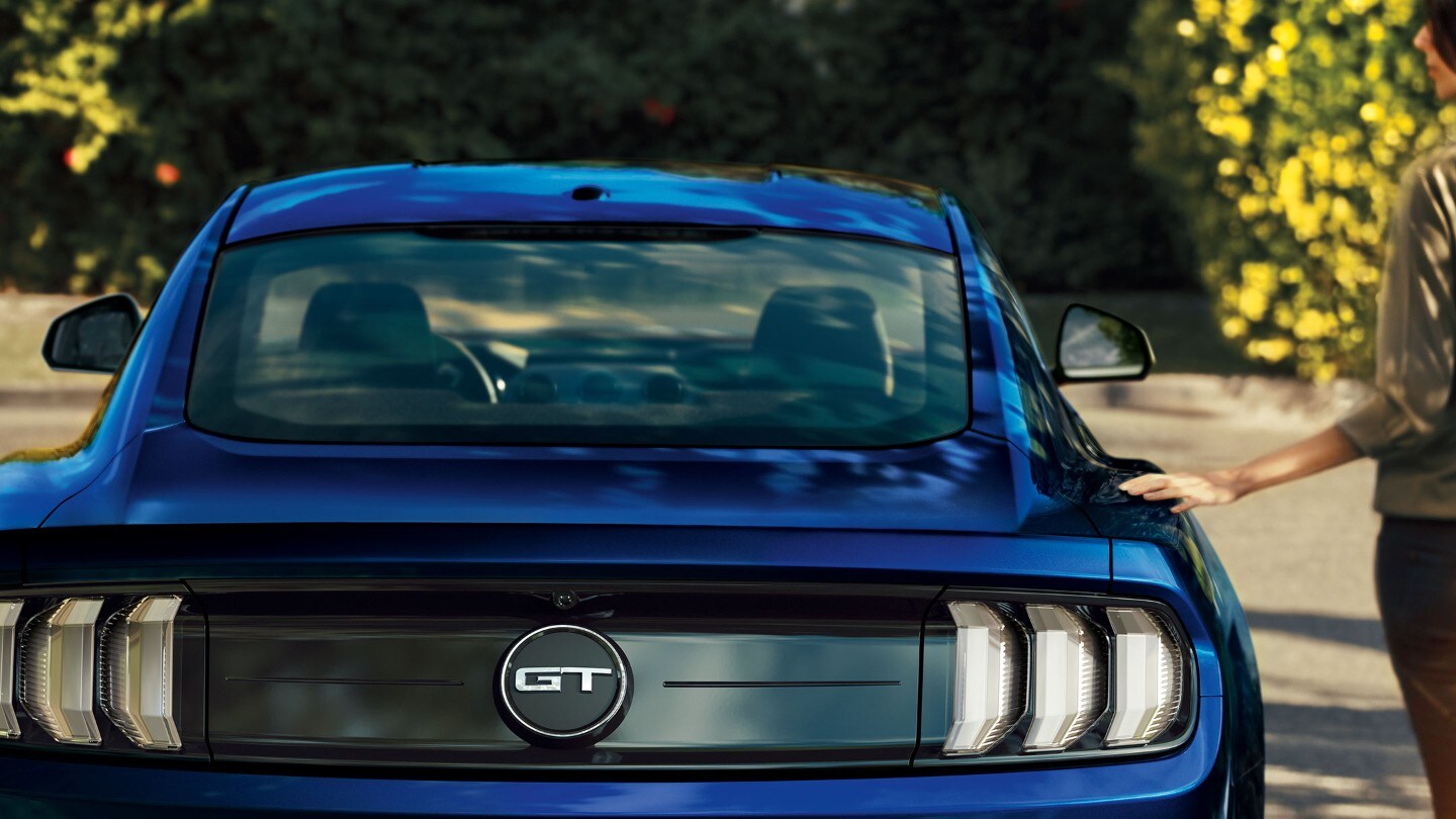 Ford Mustang GT in Blau. Heckansicht, eine Frau danebenstehend
