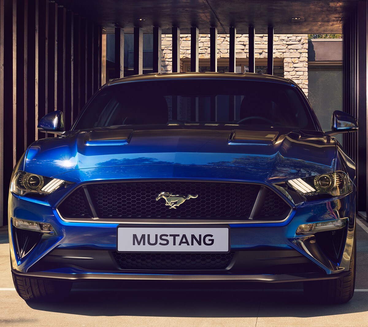 Ford Mustang in Blau. Frontansicht, parkend vor einem Metalltor