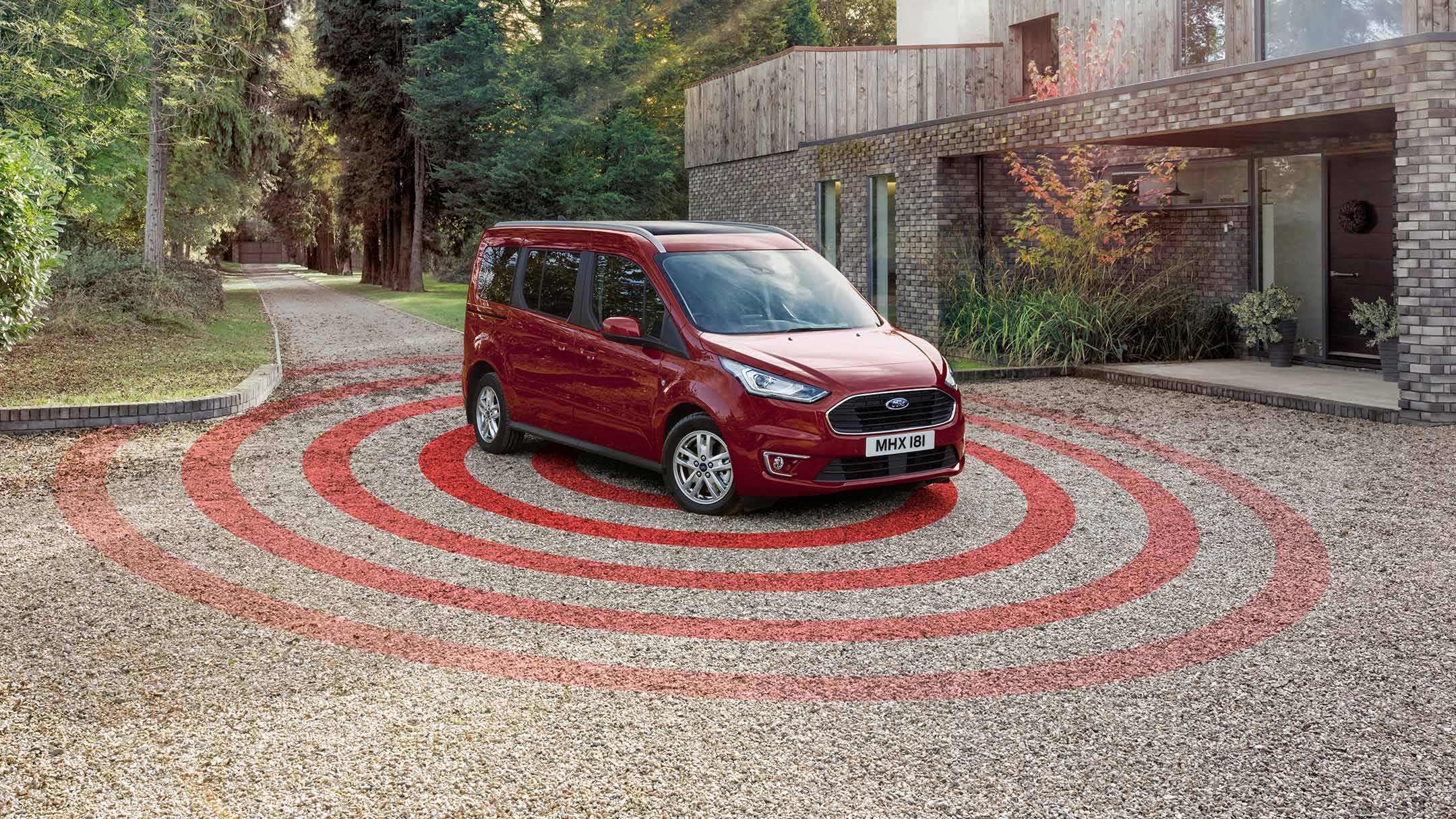 Ford Tourneo Connect in Rot. Dreiviertelansicht, parkt auf Kiesweg vor Wohnhaus mit Diebstahl-Alarmanlage Illustration