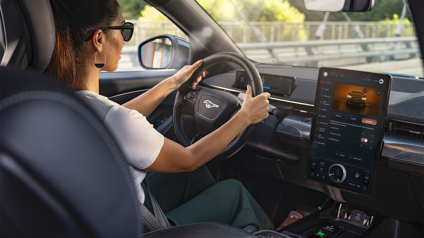 Ford Mustang Mach-E. Innenraumansicht, eine Frau betrachtet den Ford SYNC 4-Touchscreen.