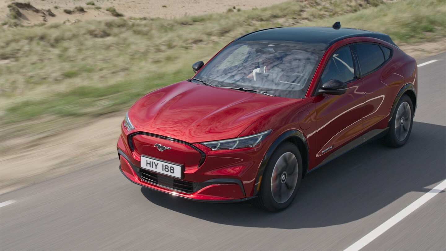 Ford Mustang Mach-E AWD in Rot. Dreiviertelansicht von vorne, fahrend auf einer Landstraße