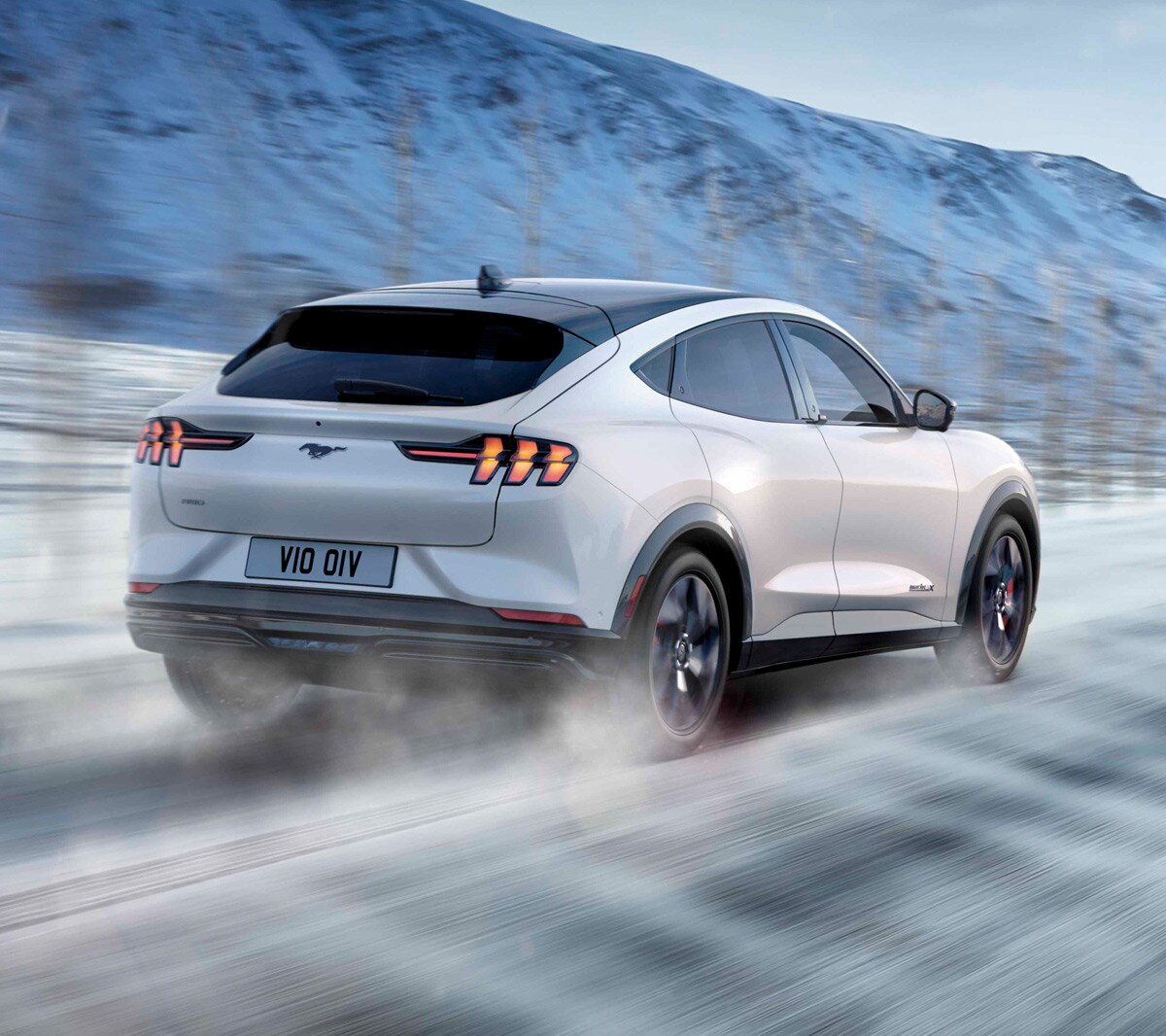 Ford Mustang Mach-E in Weiß. Dreiviertelansicht von hinten, fahrend in einer Schneelandschaft