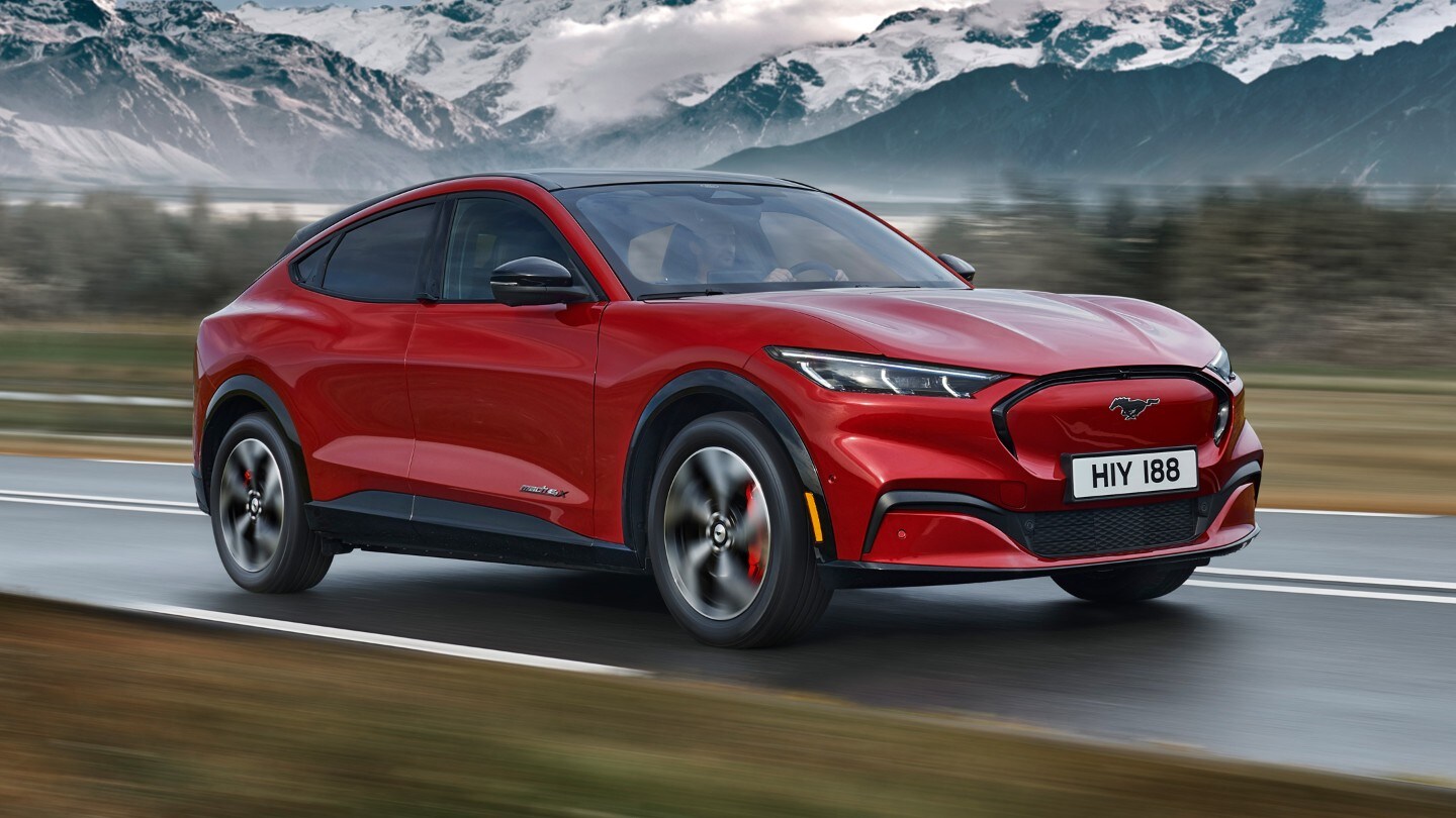 Ford Mustang Mach-E in Rot. Dreiviertelansicht von vorne, fahrend auf einer Bergpanoramastraße