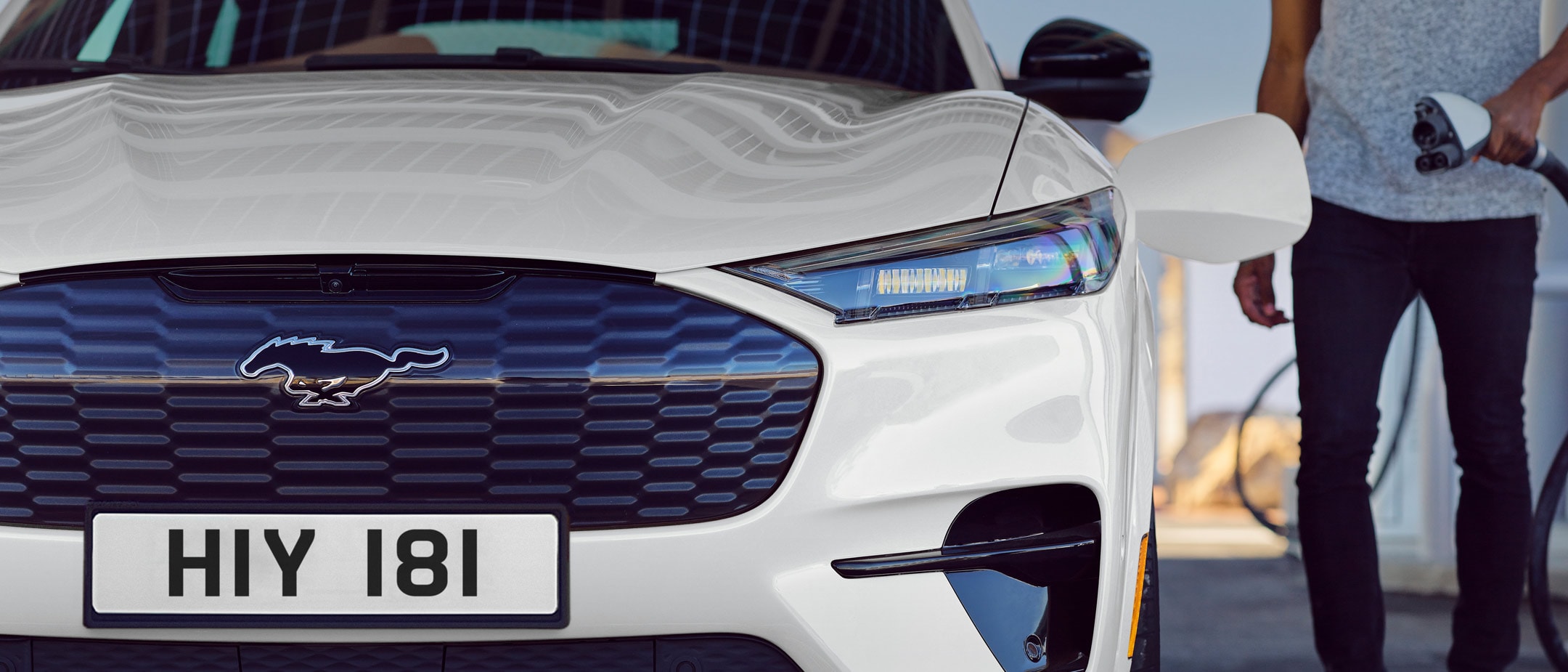 Ford Mustang Mach-E GT in Weiß. Frontansicht, Mann schließt Ladekabel an.