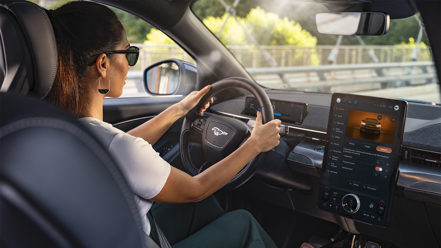 Ford Mustang Mach-E. Innenraumansicht, eine Frau betrachtet den Ford SYNC 4-Touchscreen.