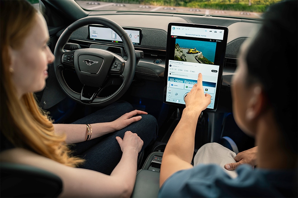 Nahaufnahme des Armaturenbretts eines Mustang Mach-E, ein Fahrer zeigt auf den Touchscreen.