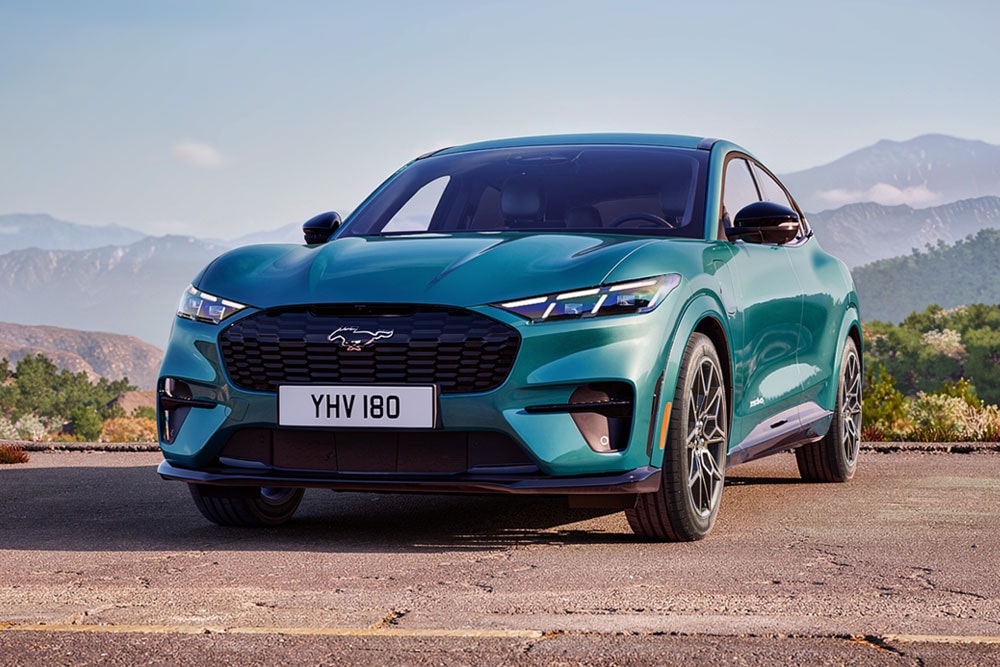 Ford Mustang Mach-E in Blau. Frontansicht, parkt vor einer bergigen Landschaft.