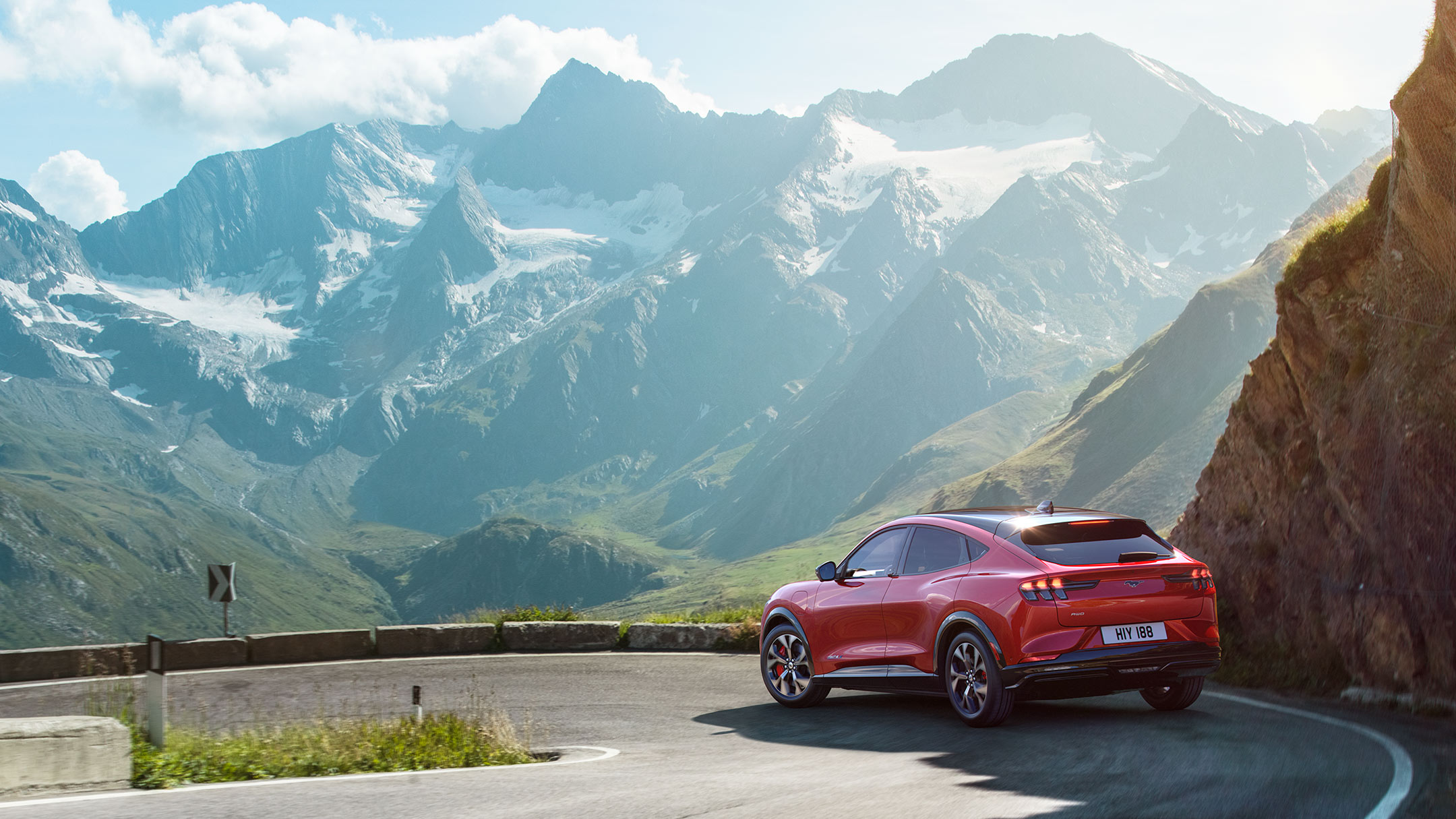 Ford Mustang Mach-E in Rot. Dreiviertelansicht von hinten, fahrend auf einer kurvigen Bergpanoramastraße