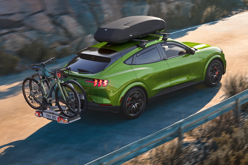 Ford Mustang Mach-E in Grün mit Fahrradträger. Fährt auf einer Bergstraße.