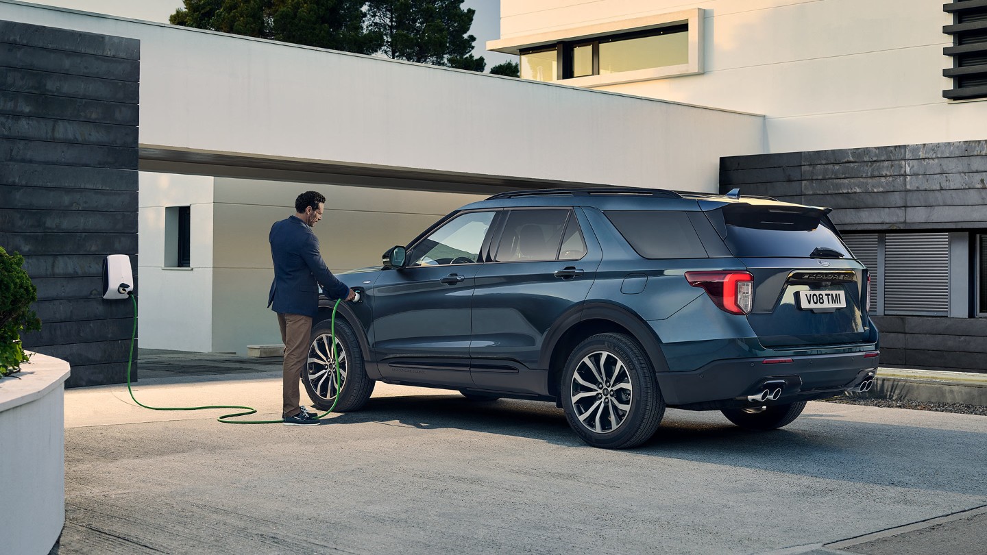 Ford Explorer Plug-in-Hybrid in Blau. Heckansicht, Ladevorgang vor einem Gebäude