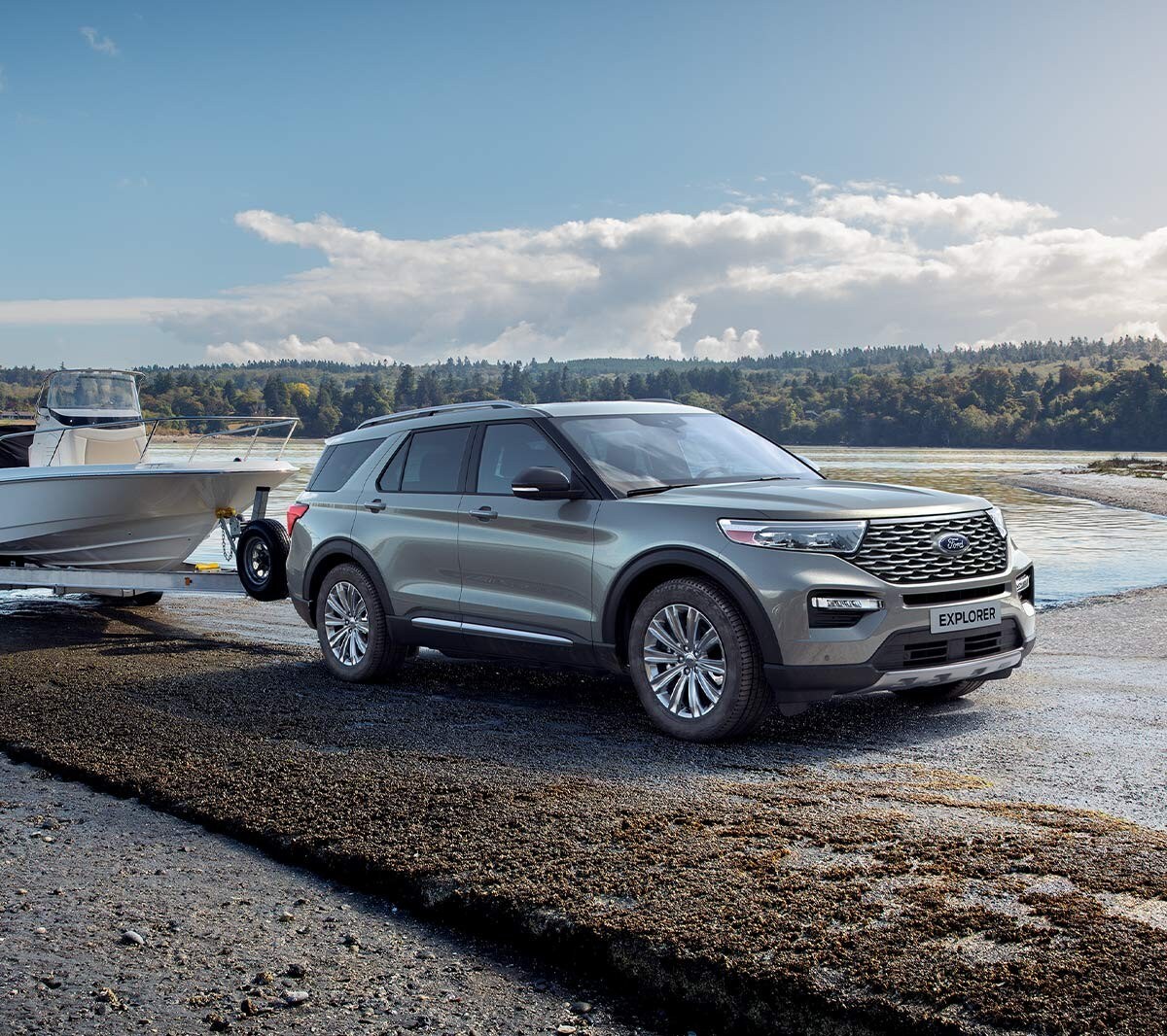 Ford Explorer Plug-in-Hybrid in Silber. Dreiviertelansicht von vorne, parkend mit einem Bootsanhänger an einem See