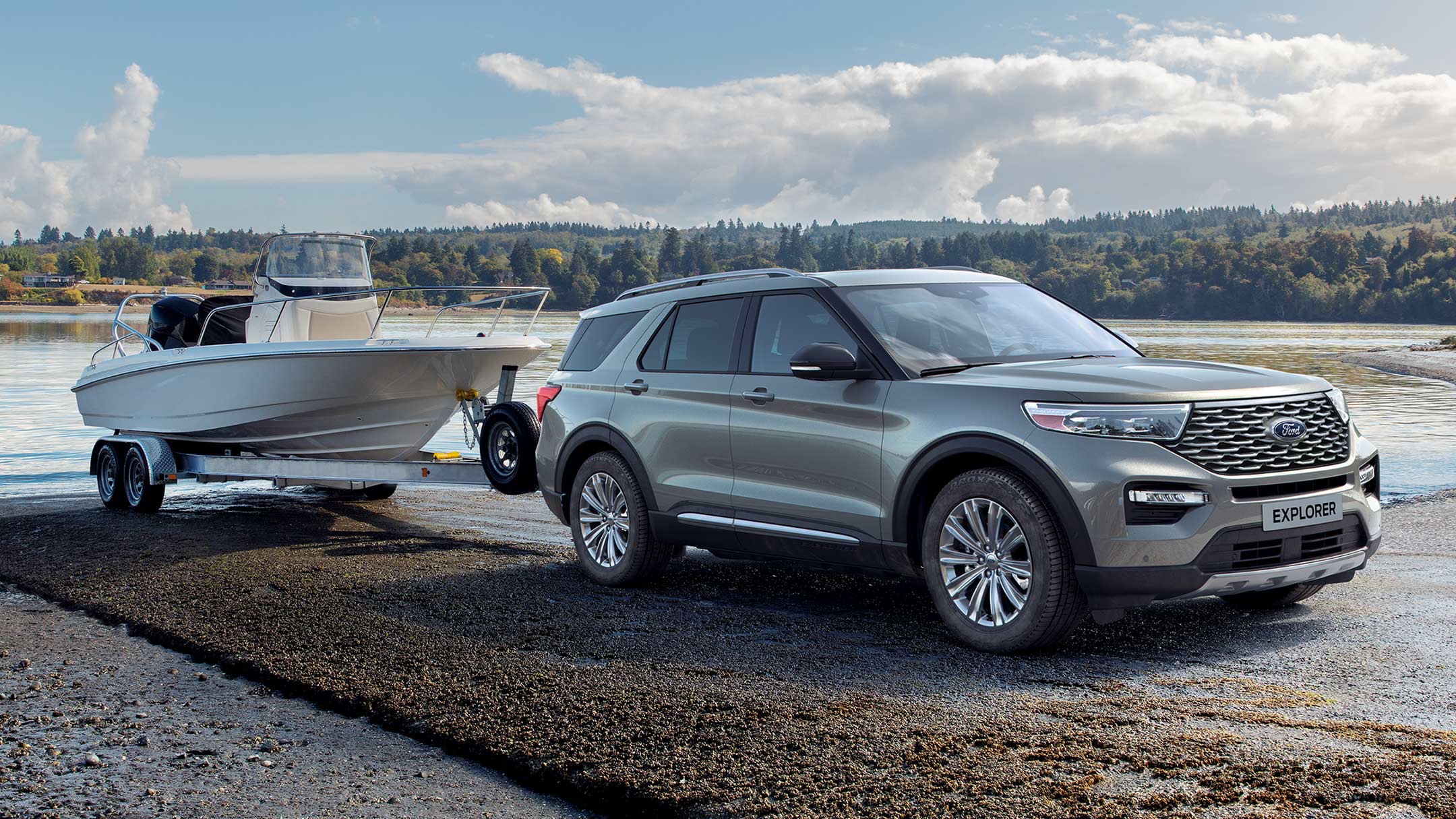 Ford Explorer Plug-in-Hybrid in Silber. Dreiviertelansicht von vorne, parkend mit einem Bootsanhänger an einem See