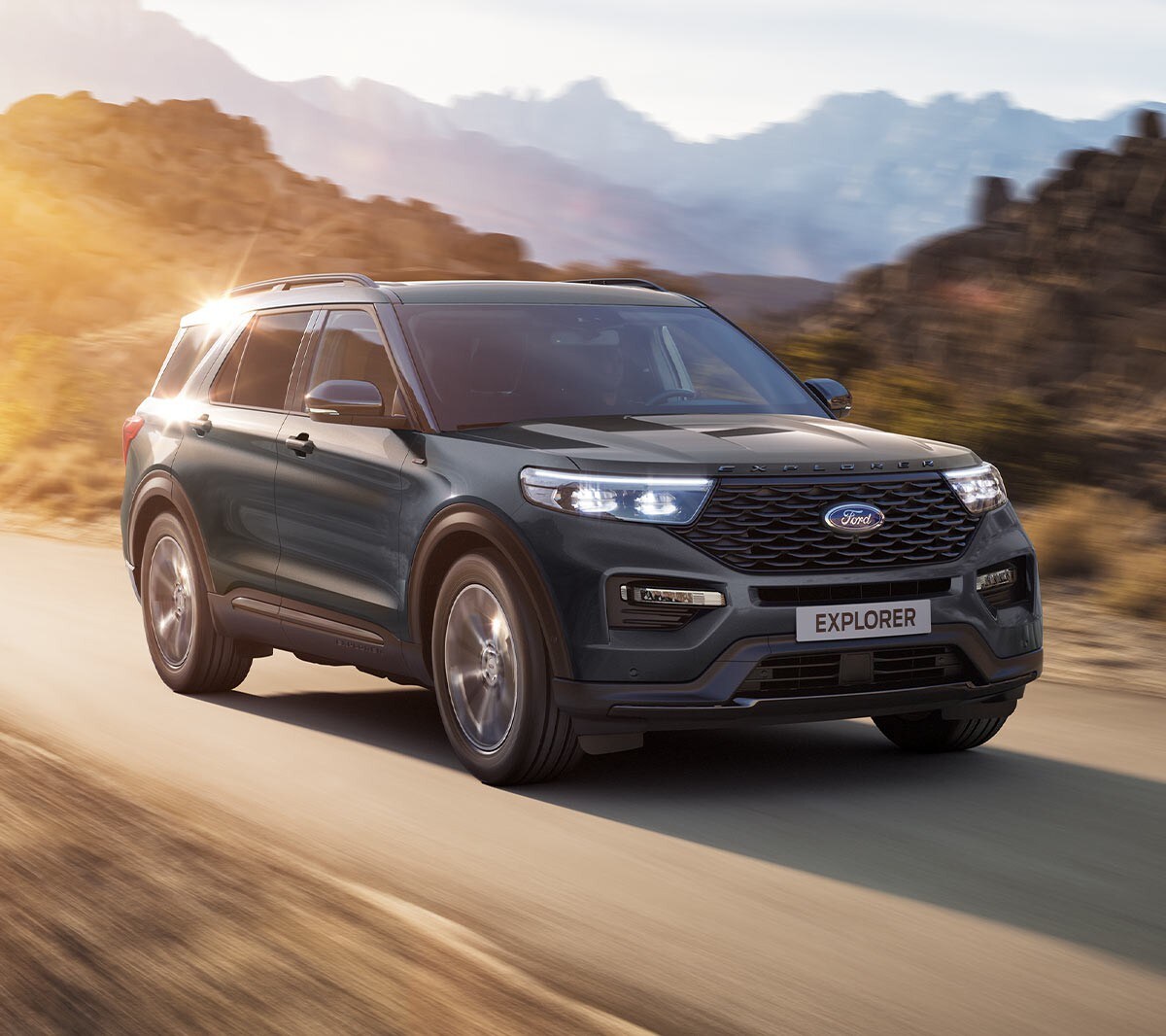 Ford Explorer Plug-in-Hybrid in Blau. Dreiviertelansicht, fahrend auf einer Landstraße mit Bergen im Hintergrund