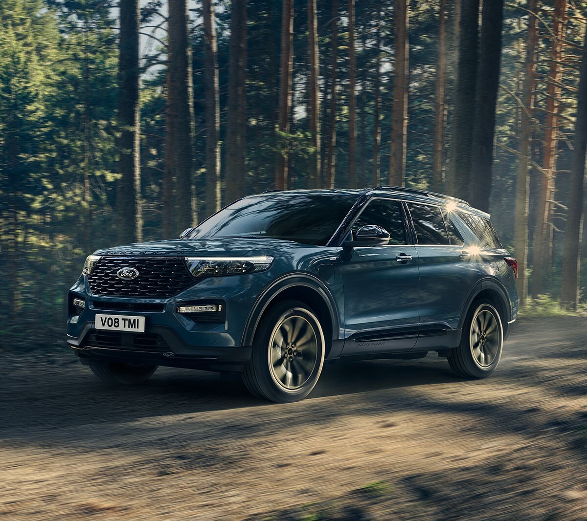 Ford Explorer Plug-in-Hybrid in Blau. Dreiviertelansicht von vorne, fahrend auf einer Landstraße mit Wald im Hintergrund