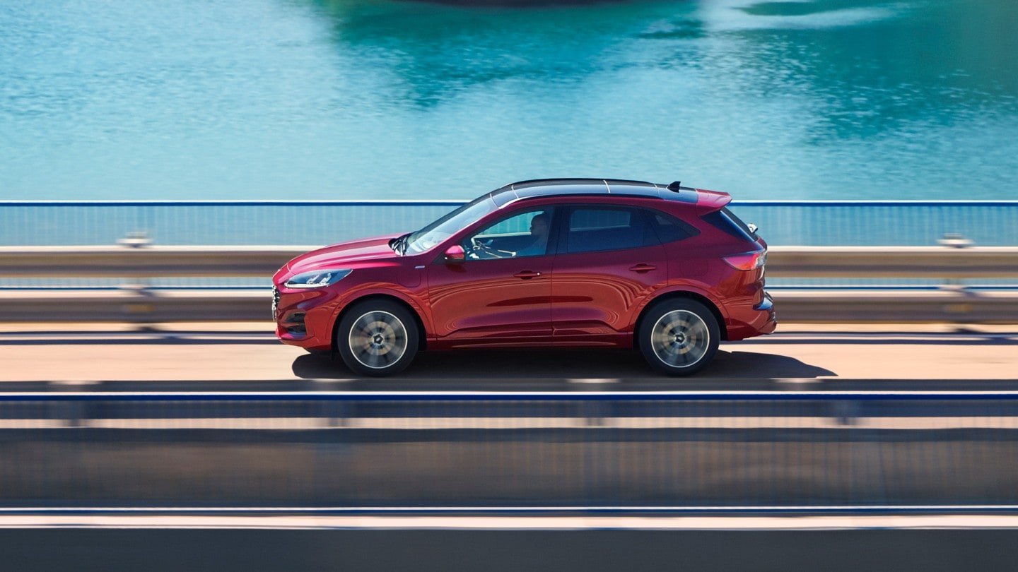 Ford Kuga in Rot. Seitenansicht, auf einer Brücke fahrend