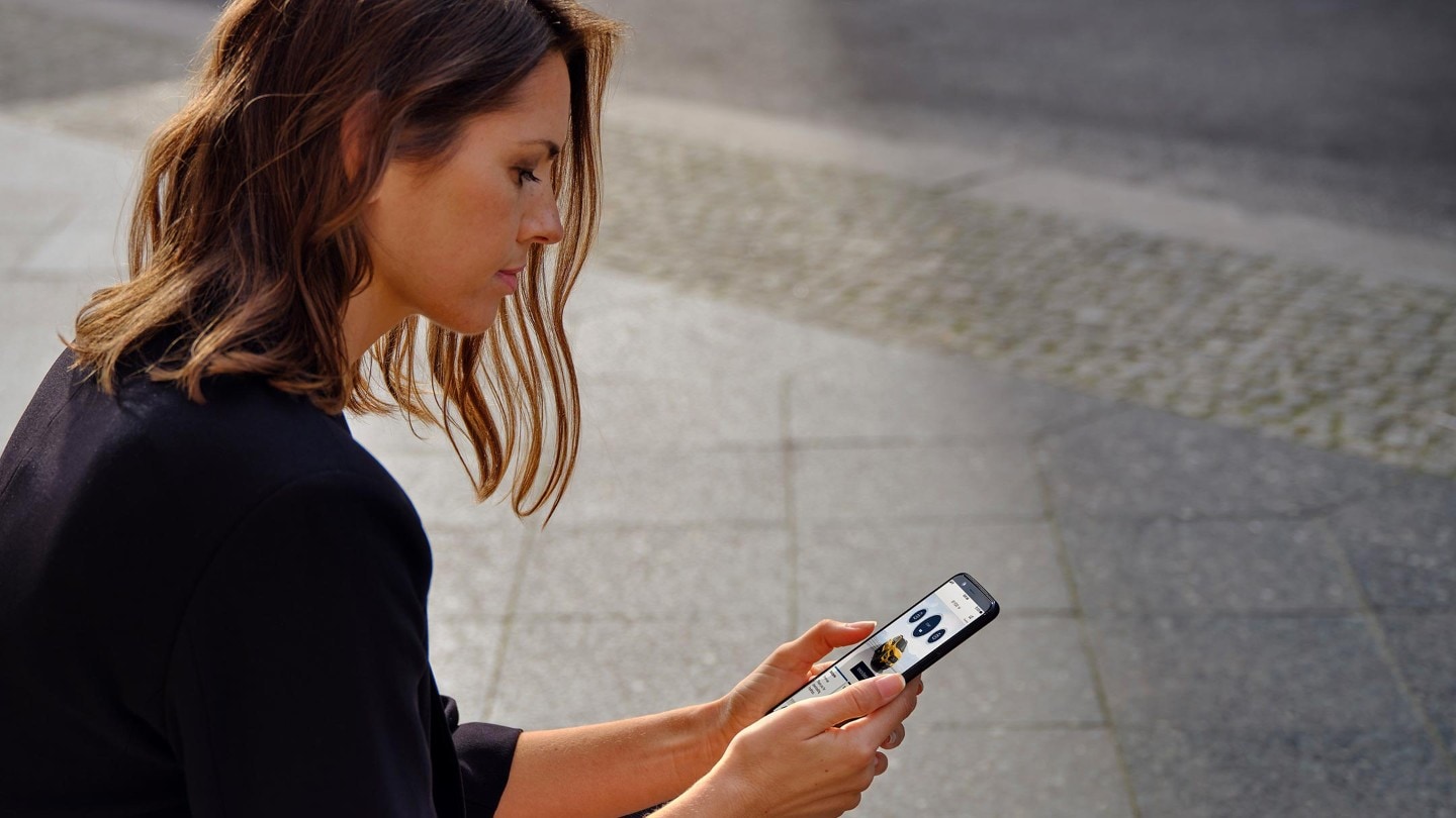 Frau am Straßenrand sitzend und auf ihr Smartphone blickend