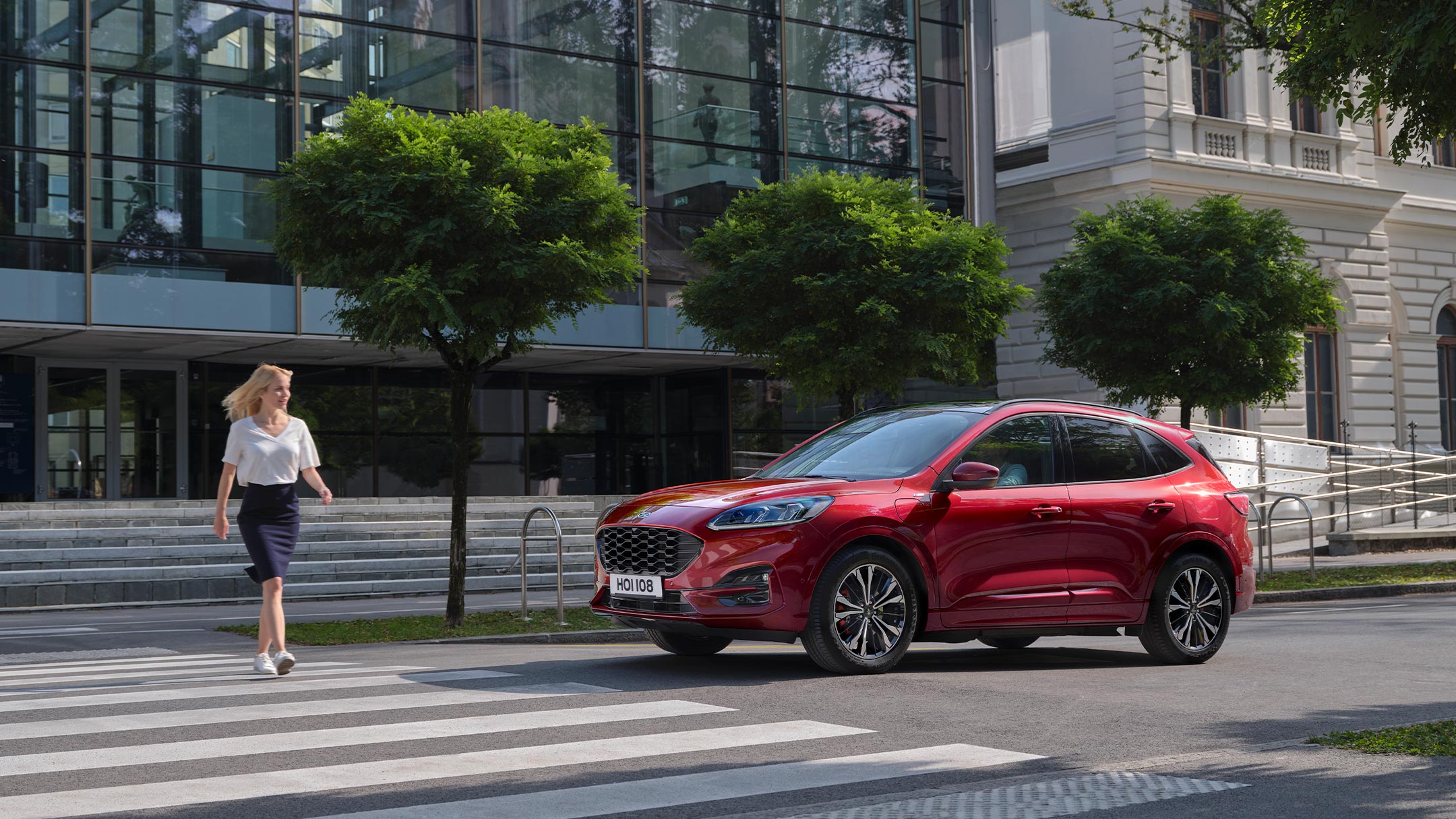 Ford Kuga in Rot. Seitenansicht, stehend vor einem Zebrastreifen in der Stadt