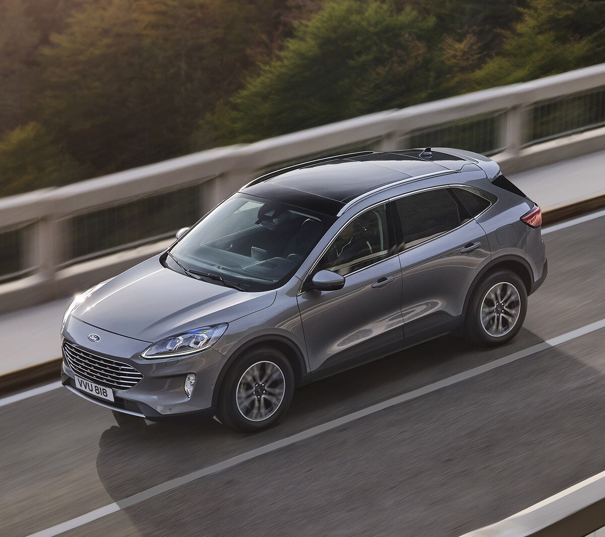 Ford Kuga in Grau. Dreiviertelansicht von oben, fahrend über eine Brücke mit Wald im Hintergrund