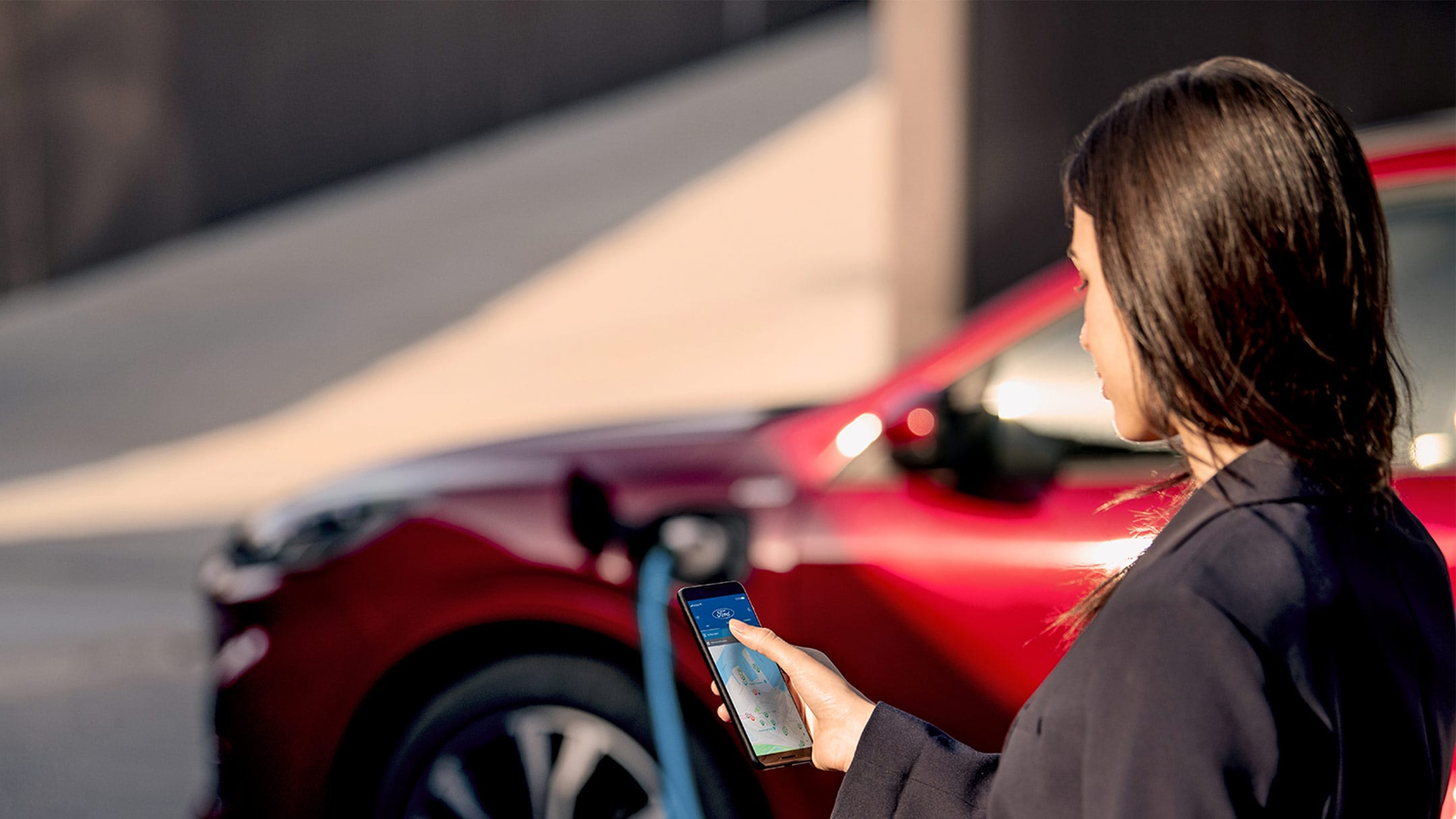 Frau die auf ihr Handy sieht, während sie ihren Ford auflädt