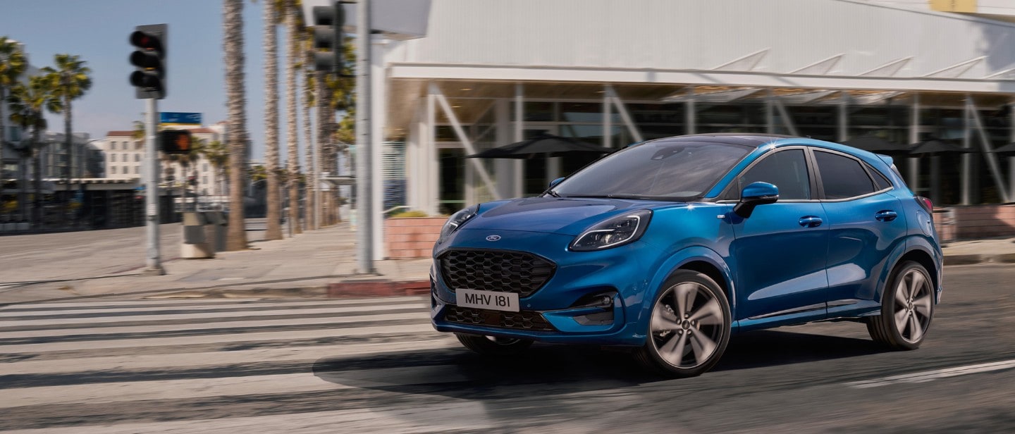 Ford Puma in Blau. Dreiviertelansicht, auf einer Straße mit Palmen im Hintergrund